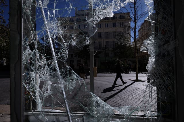 A person walking along a street is seen through a broken billboard days after nationwide protests against the cost of living and rising fuel prices called by the "Yellow Vests" movement and ahead of a second round of demonstrations, in Marseille, France, October 21, 2026.