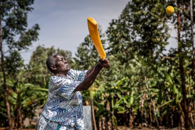 An elderly woman plays a shot during a cricket and physical training session in Jinja