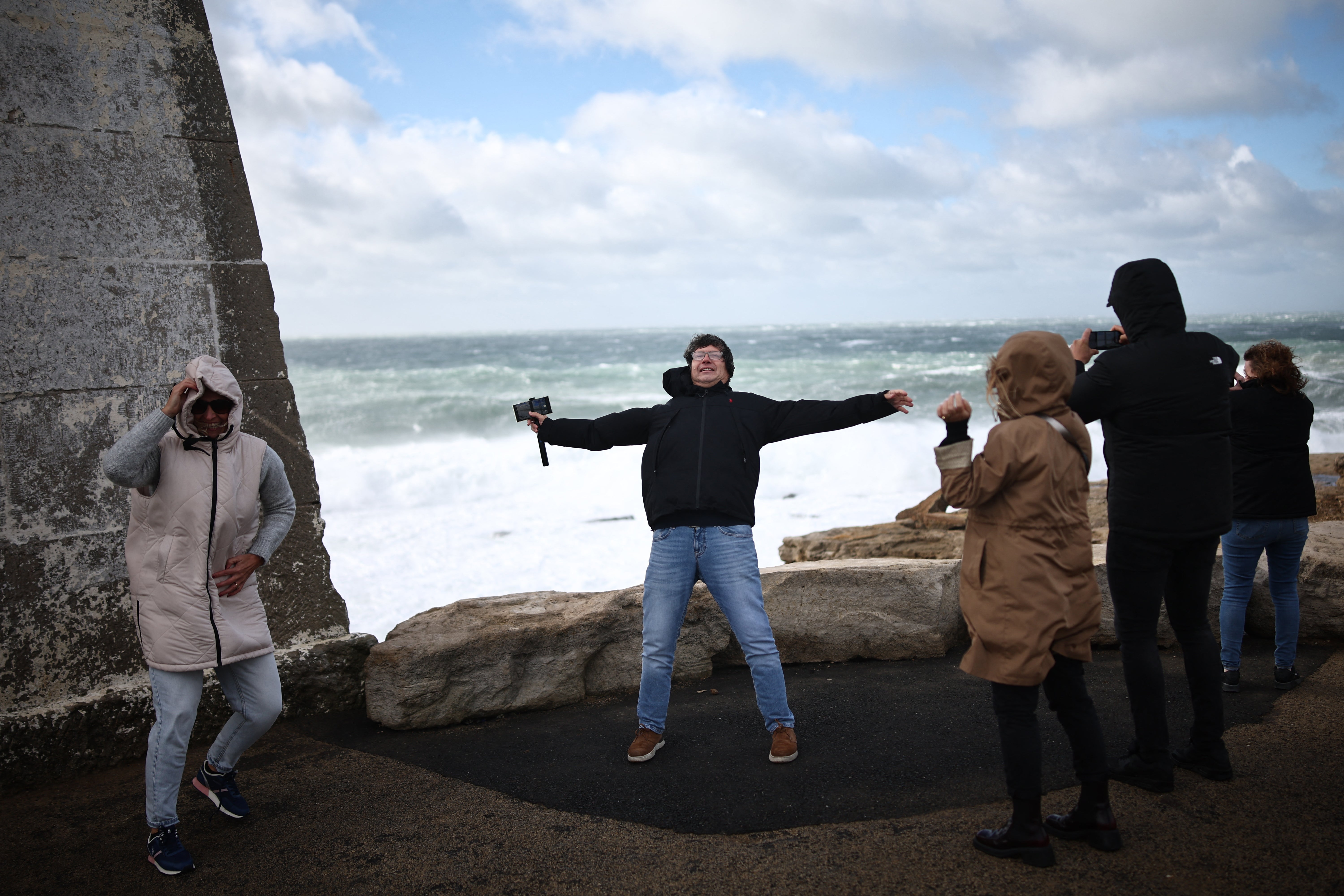 Members of the public brace themselves against the strong winds beside the breaking waves at Portland Bill, southern England on October 23, 2026, as Storm Austen brings strong winds and heavy rain across much of southern England
