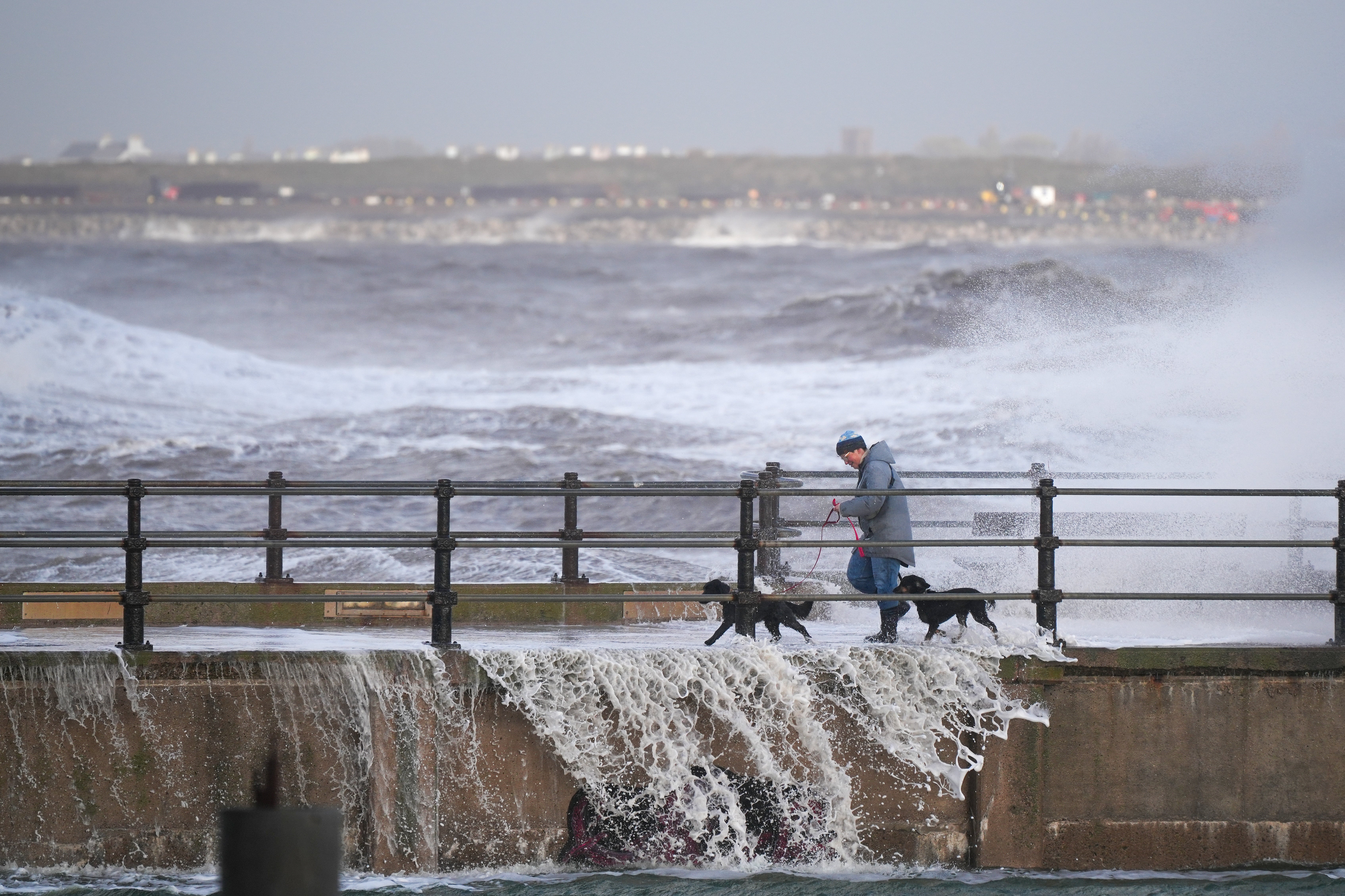 A person walks their dogs along the sea wall as waves created by the high winds of Storm Boelo hit the sea wall at New Brighton promenade