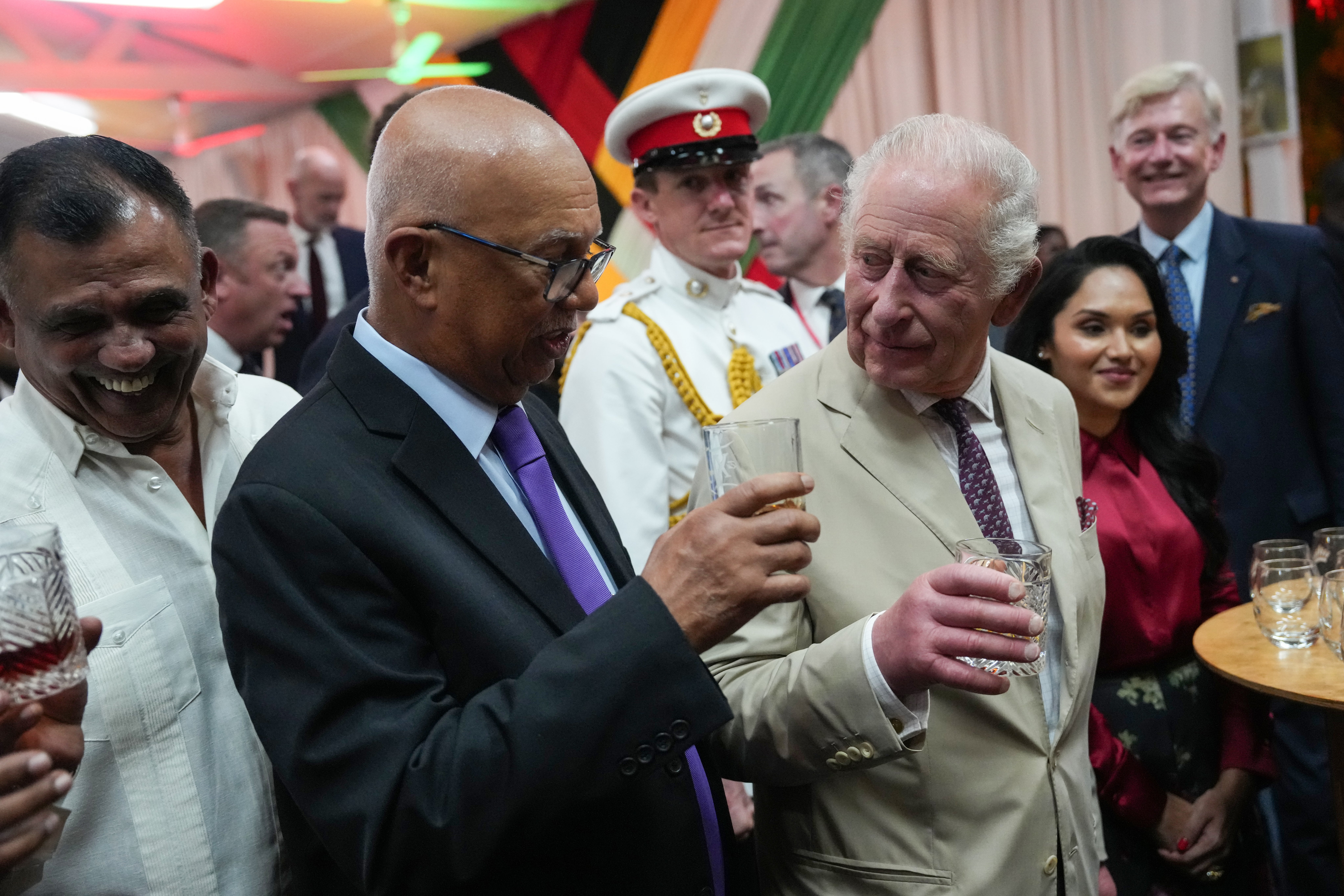 King Charles III (R) holds a glass of a special Guyanese rum created in his honour alongside guests during a State Reception
