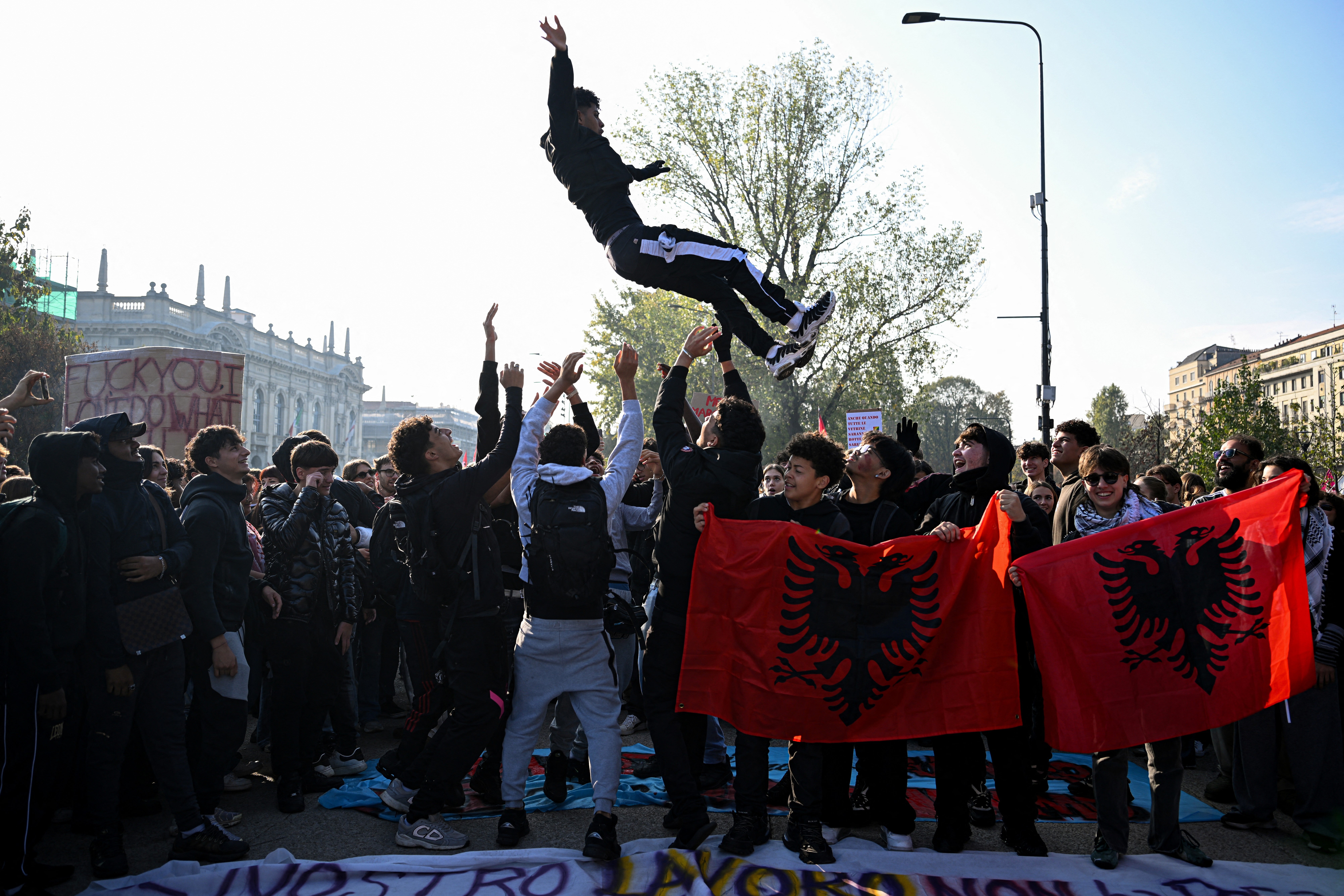 Protesters throw one of their peers into the air and hold Albanian national flags near the Politecnico di Milano university in Milan