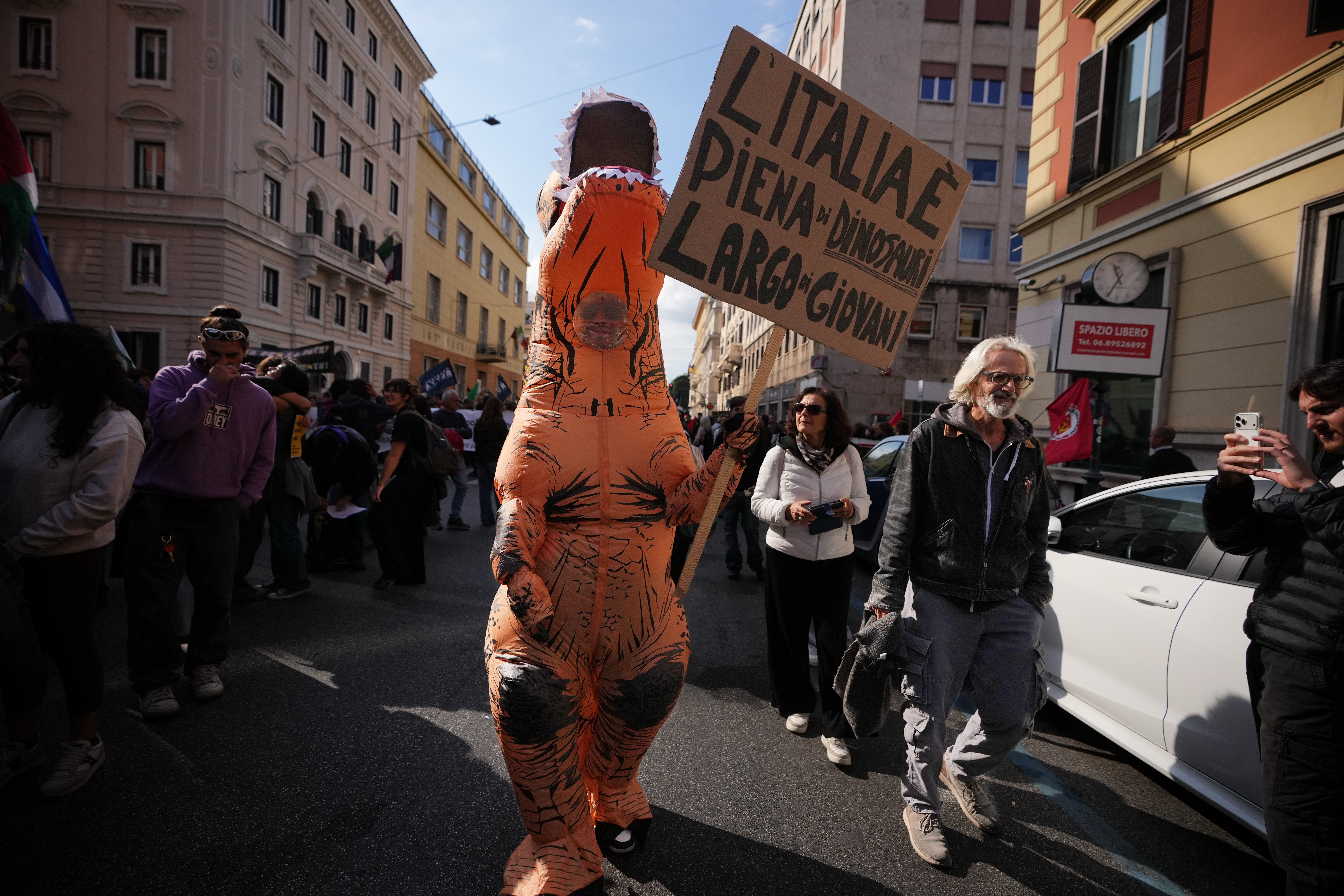 A demonstrator dressed as a dinosaur holds a placard reading 
