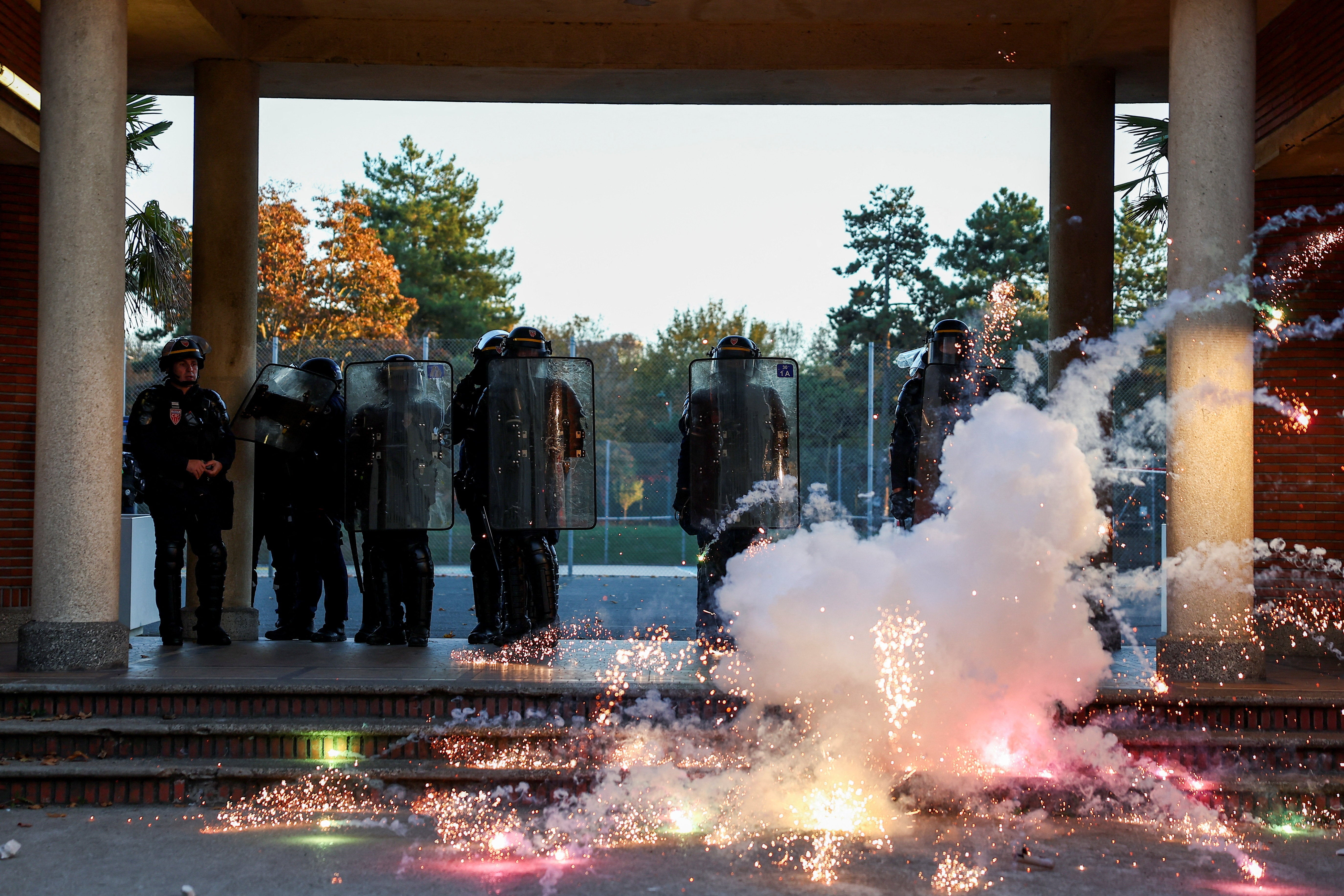 A pyrotechnic explodes next to police officers in riot gear in the French capital