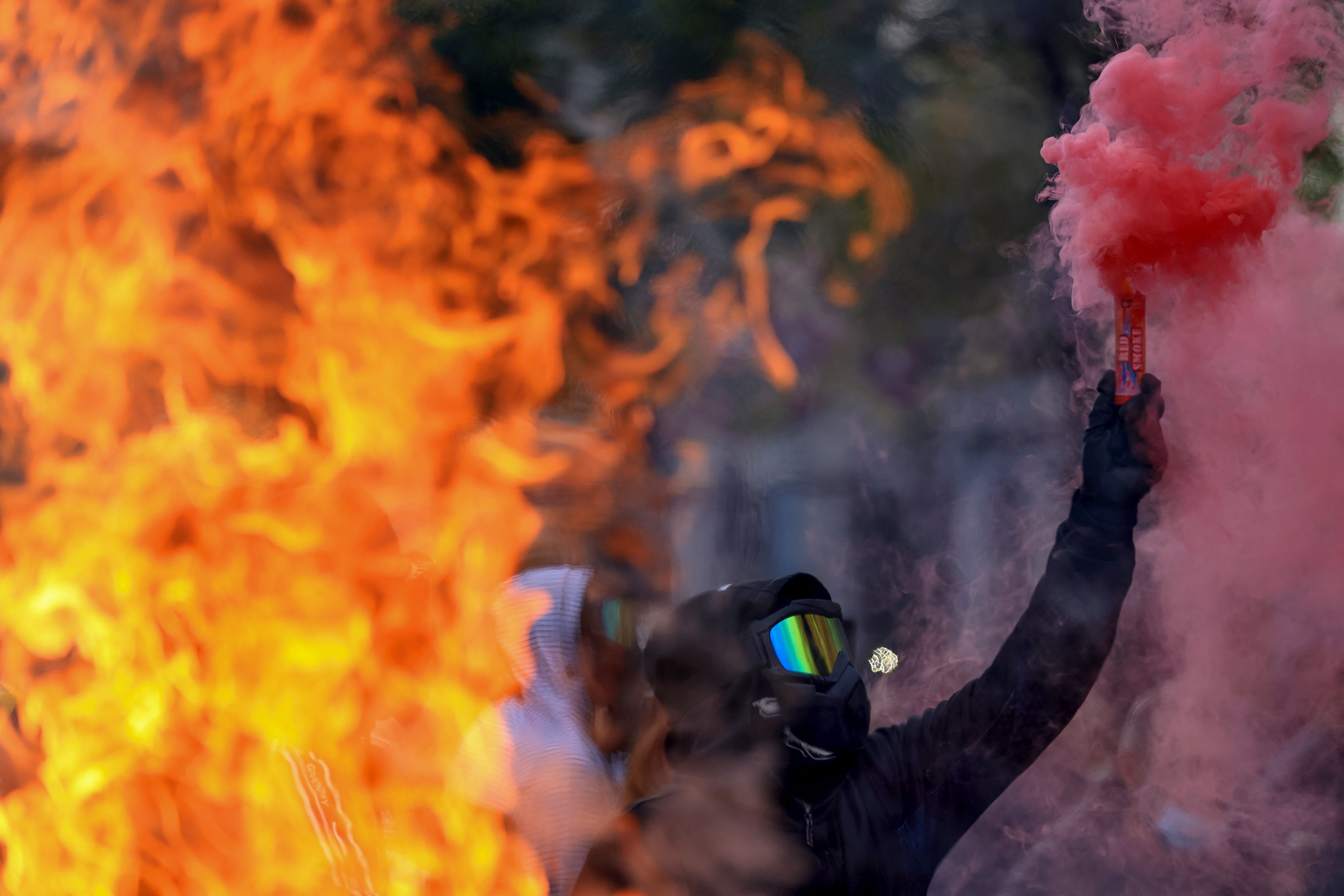 A protester holds a smoke bomb with flames in the foreground during an anti-government demonstration in central Tirana, Albania