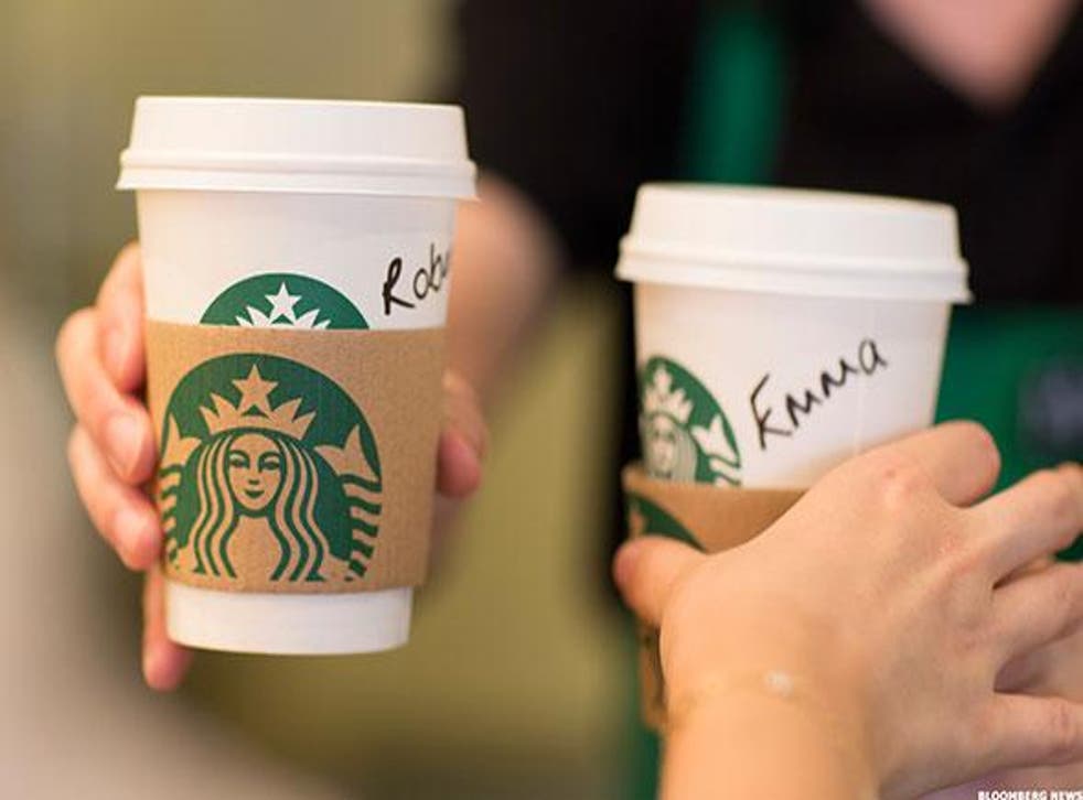 An employee hands a customer personalised cardboard coffee cups inside a Starbucks