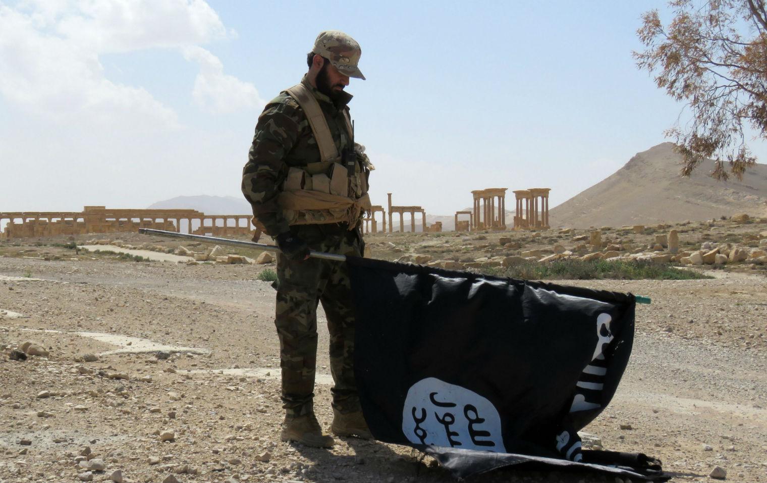 A member of the Syrian pro-government forces carries an Isis flag in Palmyra on 27 March 2016