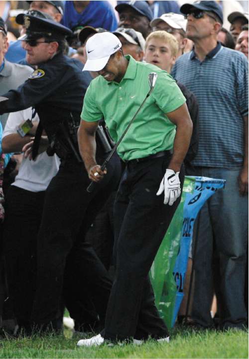 Woods, who is suffering from a left knee injury, grimaces in pain after hitting from the rough on the first fairway