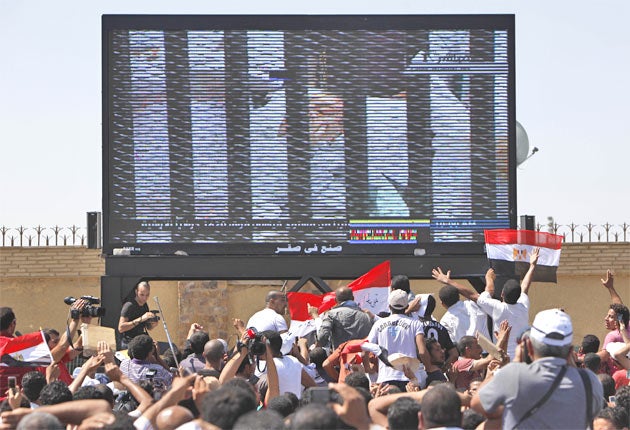 Hosni Mubarak is seen on a huge TV screen outside the Police Military Academy in Cairo, as the former Egyptian president enters the courtroom on a hospital bed