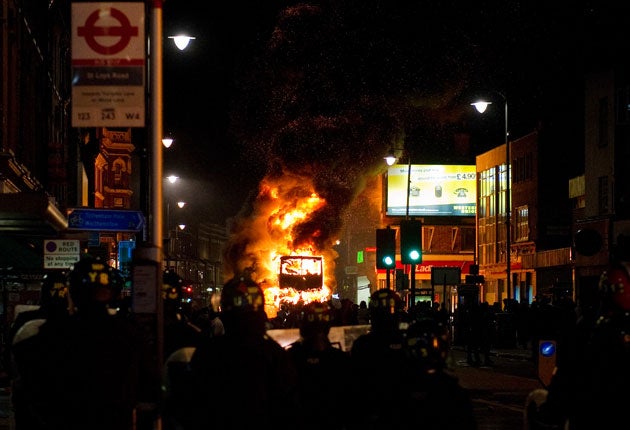 A double decker bus burns as riot police try to contain a large group of people on a main road in Tottenham, north London
