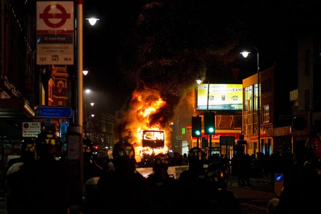 A double decker bus burns as riot police try to contain a large group of people on a main road in Tottenham, north London