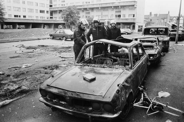 Police in riot gear inspect a burned-out car on the Broadwater Farm estate in October 1985
