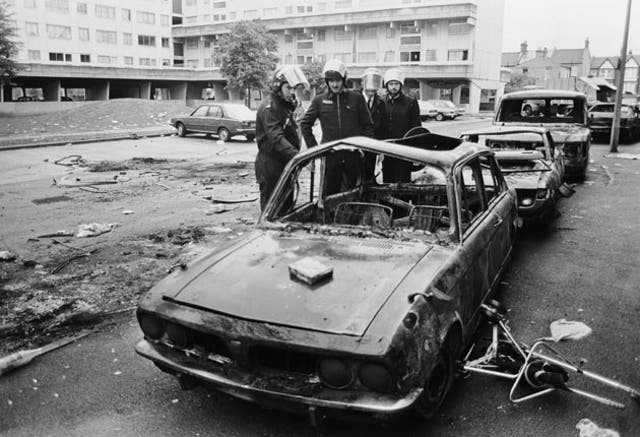 Police in riot gear inspect a burned-out car on the Broadwater Farm estate in October 1985