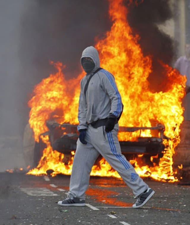 A masked rioter is seen in front of a burning car in Hackney, East London