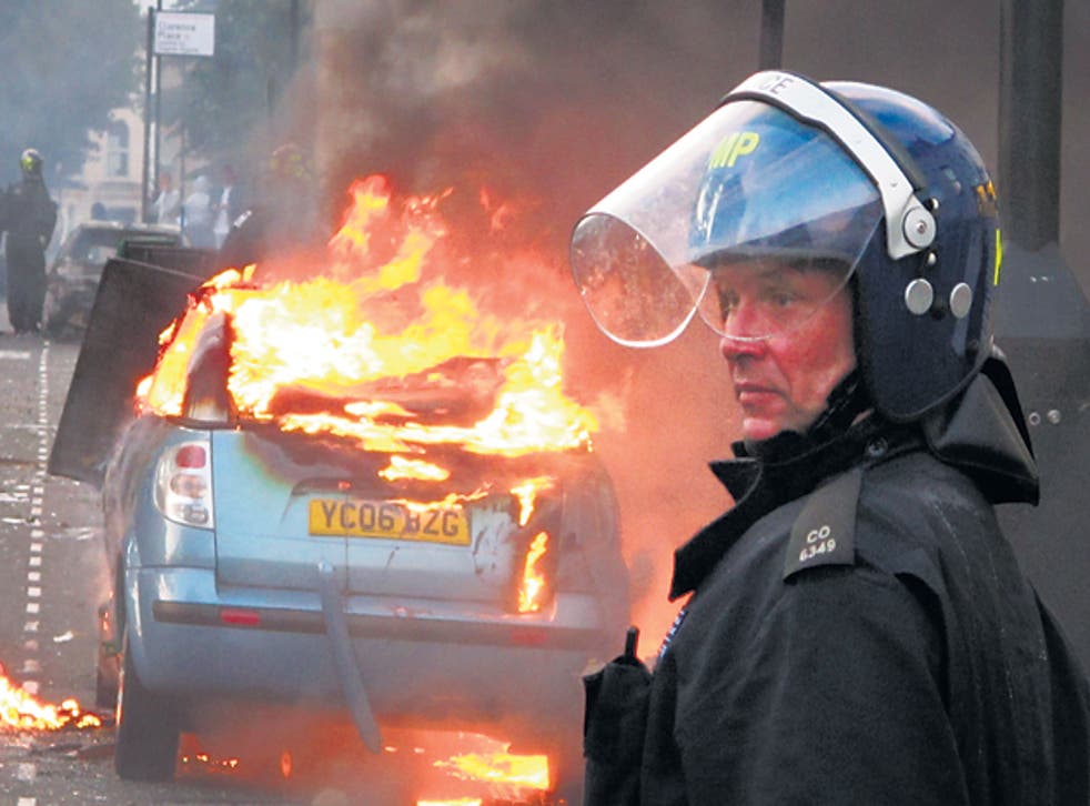A police officer in riot gear stands near a burning car in Hackney