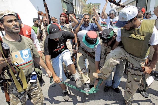 Rebel fighters tear a green Gaddafi-era Libyan flag to shreds after storming the women's army barracks in Tripoli yesterday