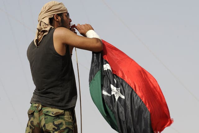 A rebel fighter puts up the new Libyan flag at a checkpoint