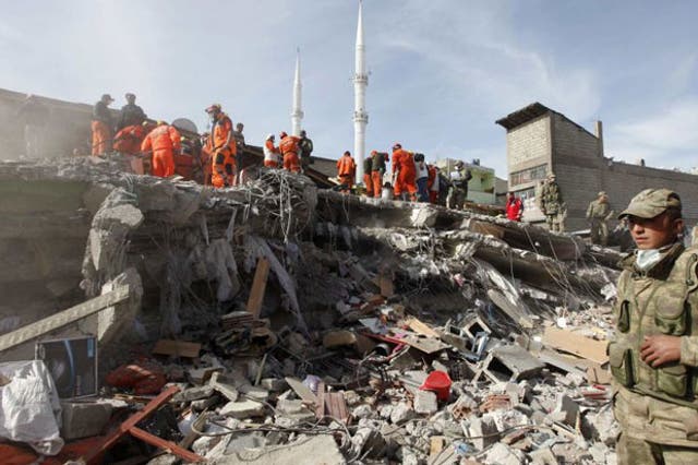 Soldiers stand near rescue workers as they try to save people trapped under debris following the earthquake. Reuters