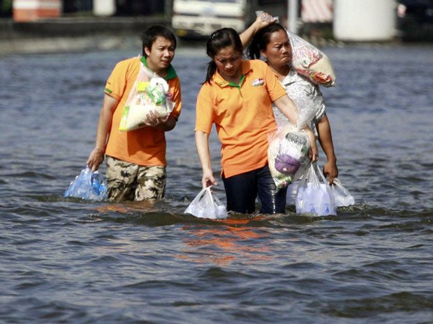 Residents carrying relief packages wade through a flooded street in Bangkok