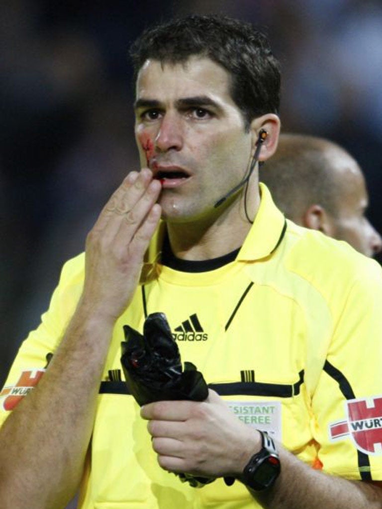 A Spanish assistant referee touches his lip as he holds an umbrella thrown from the stands