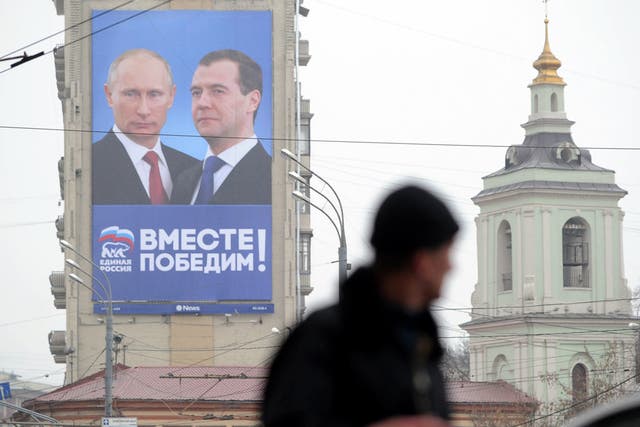 A man walks past by  a huge Parliamentary election campaign poster of the United Russia ruling party depicting President Dmitry Medvedev and Prime Minister Vladimir Putin, in Moscow