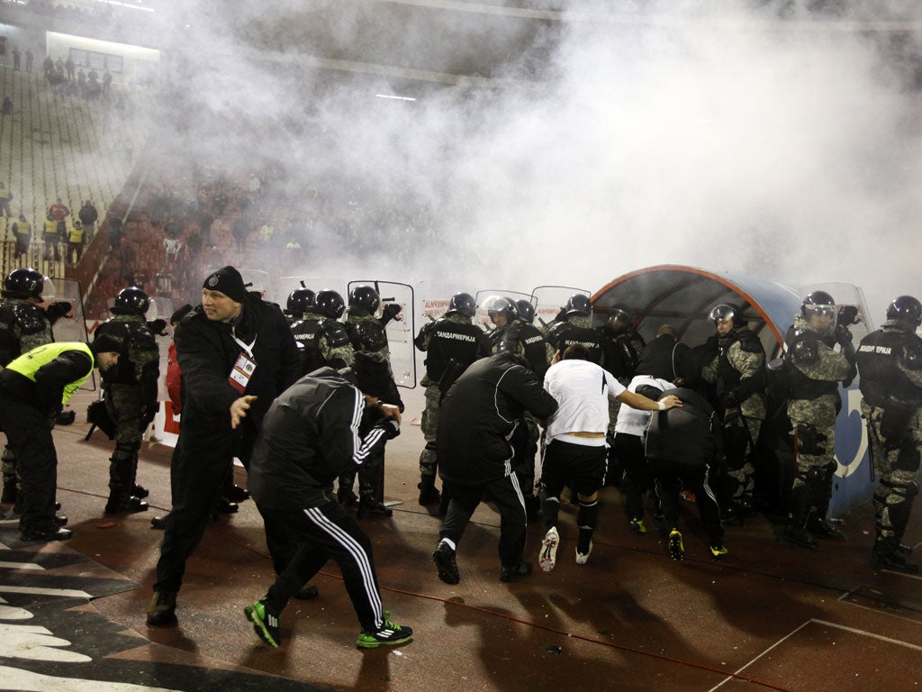 Security personnel help escort Partizan Belgrade's team players as they run from the pitch after Red Star Belgrade fans started throwing objects at them