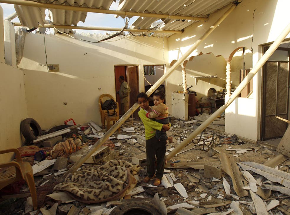 A Palestinian girl holds her brother as she looks at a house damaged in an Israeli air strike in Gaza