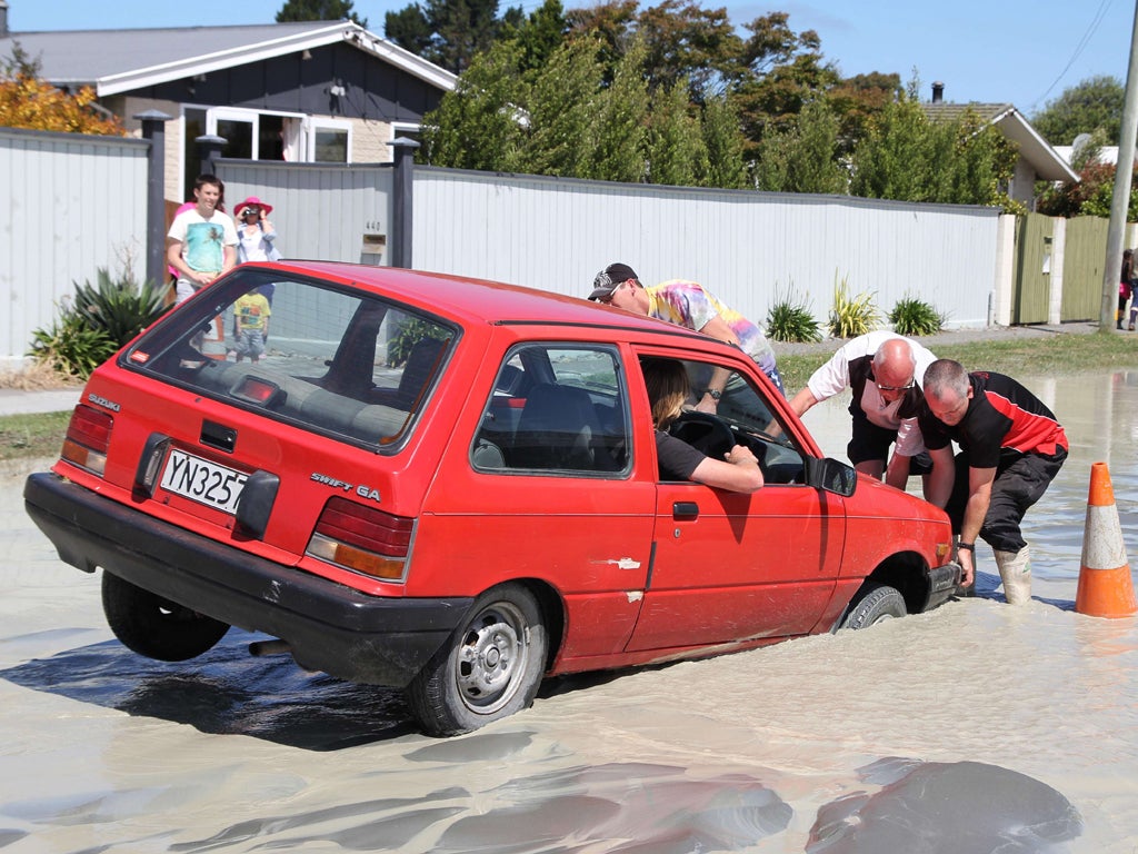 Residents try to free a car stuck in a liquefaction sink hole