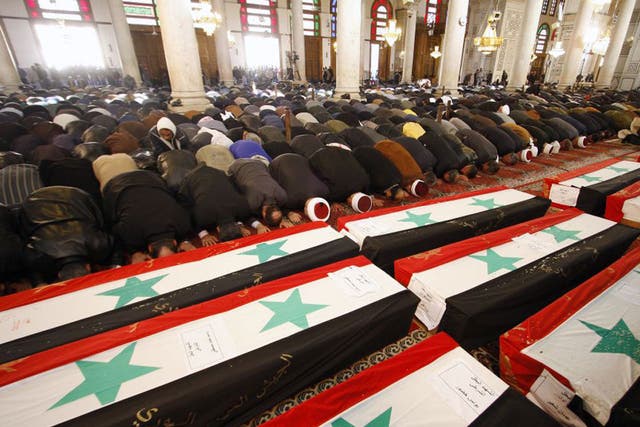 Mourners bow in prayer at a mass funeral for 44 people killed in twin suicide bombings that targeted intelligence agency compounds in Damascus