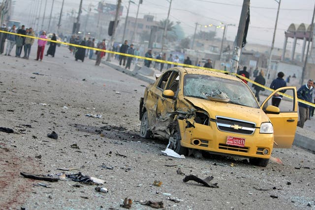 A destroyed car sits in a cordoned-off area as Iraqi security forces inspect the site of a blast after a bomb ripped through a group of workers in Sadr City in Baghdad 