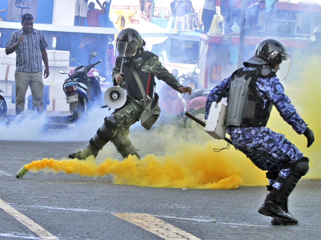 A soldier and a police officer take cover as supporters of the Maldives' ousted president hurl back a tear gas canister thrown at them in the capital, Malé