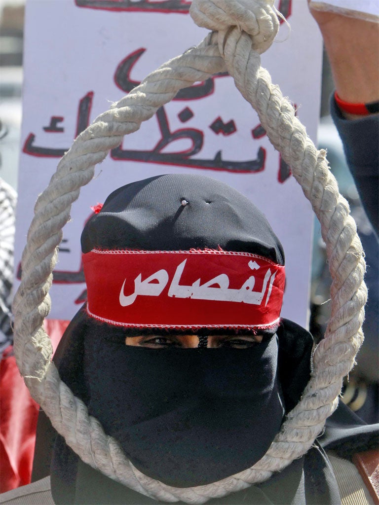 A protester wears a headband with the word 'Retribution' and holds a noose outside the court
