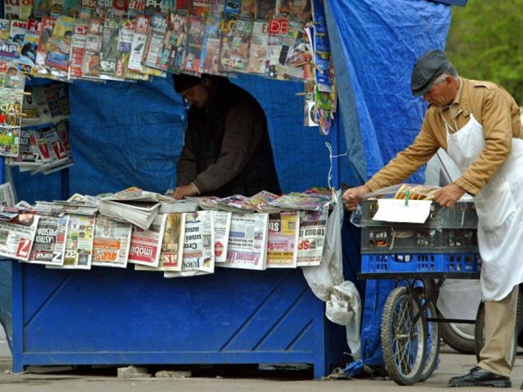 A Romanian pretzel seller arranges his wares near a newsvendor's stall in Bucharest