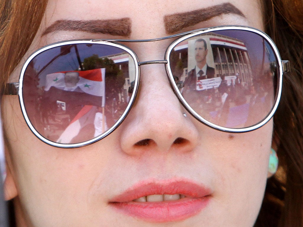 Images of President Bashar al-Assad are reflected on a woman’s sunglasses as protesters light fires and shelling continues in Homs yesterday