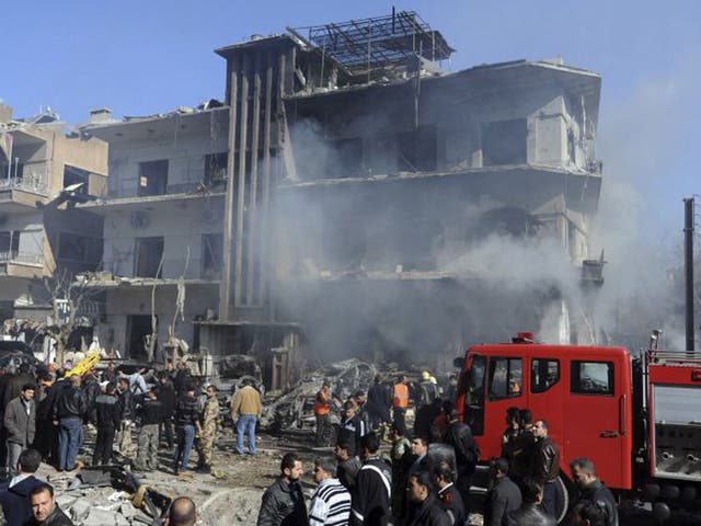In this photo released by the Syrian official news agency SANA, Syrian security forces gather in front of a damaged building near the aviation intelligence department, which was attacked by one of two explosions, in Damascus