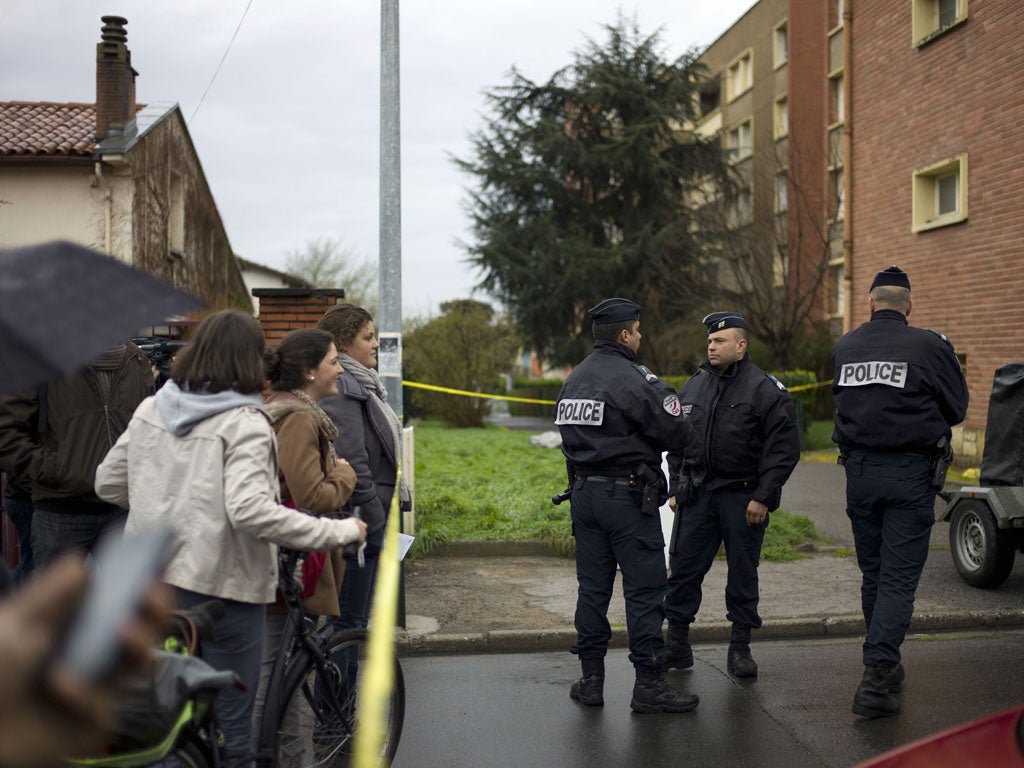 Passers by look on as French police officers block the street in front of Mohamed Merah's apartment building in Toulouse