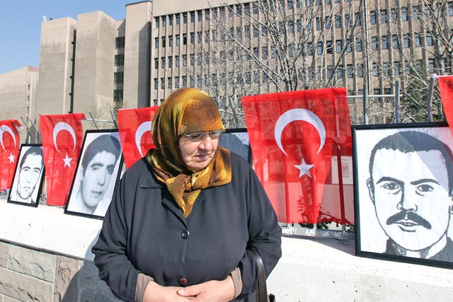 A woman stands in front of portraits of youths who were executed, died or disappeared in jails during military rule after Turkey's 1980 coup