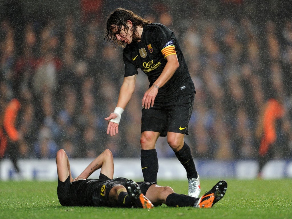Sergio Busquets on the floor as team mate Carles Puyol offers him a hand