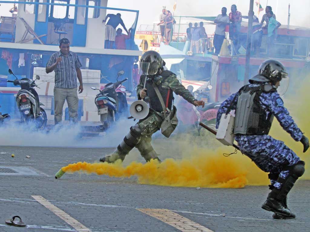A soldier and policeman take evasive action as a supporter of ex-president Nasheed hurls back a tear-gas canister