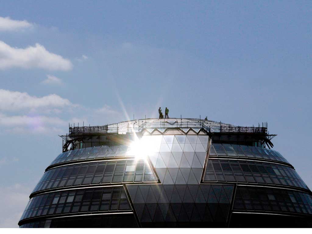 Workers install photovoltaic solar panels on the roof of London’s City Hall. But demand for them has fallen