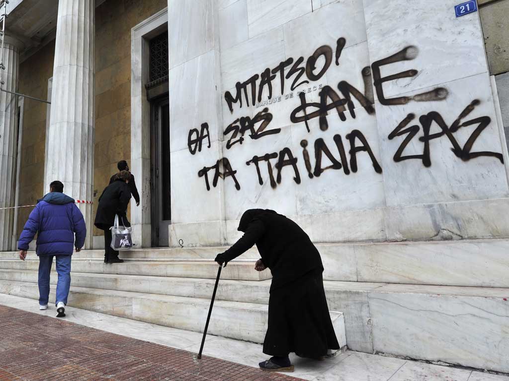 Victims of austerity: A woman begs outside an Athens bank. The graffiti reads: 'Cops, your children will eat you'