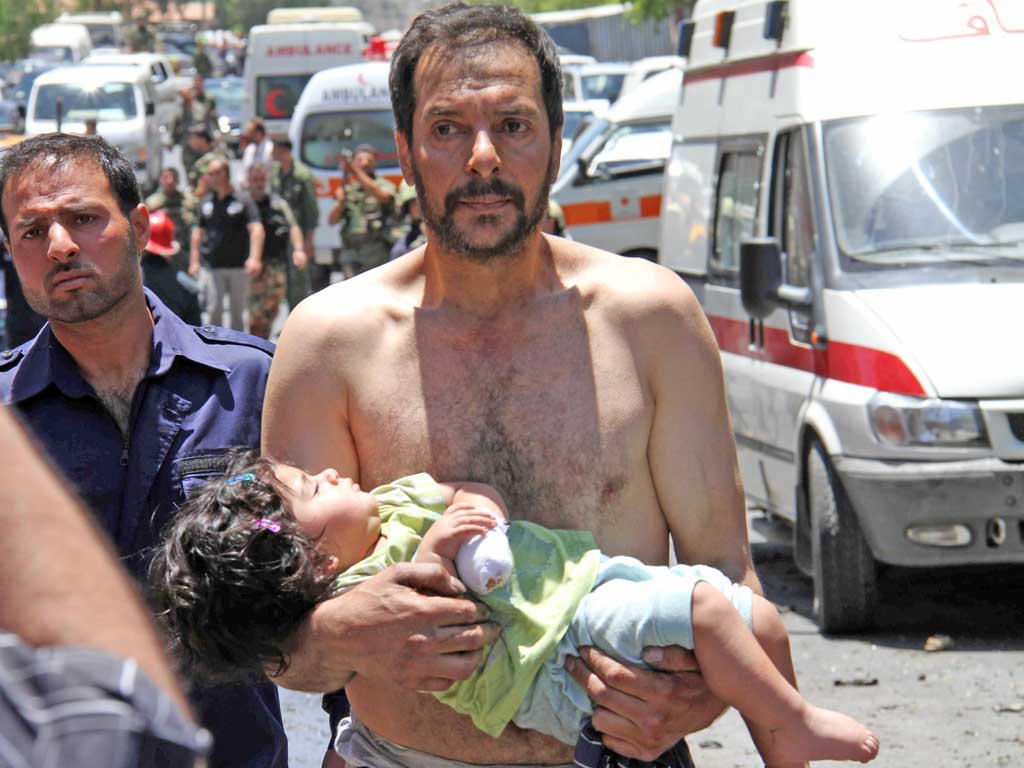 A man carries a wounded girl following an explosion that targeted a military bus near Qudssaya, a neighbourhood of the Syrian capital
