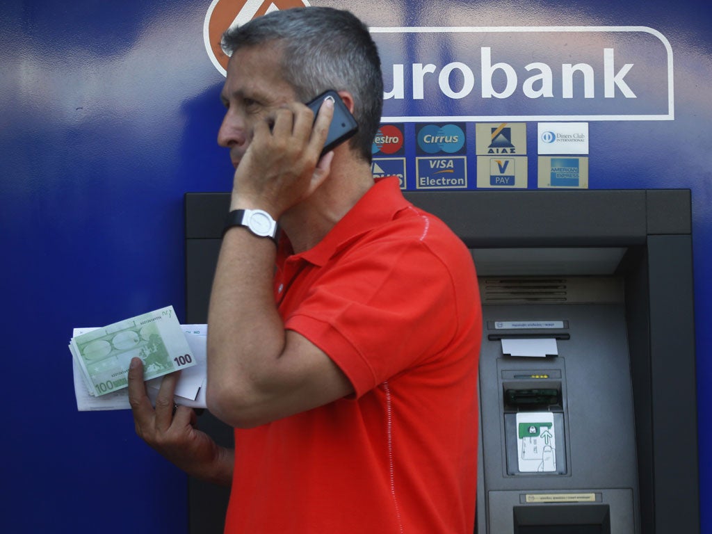 A Greek man holds 100 Euro bills which he just withdrew from a branch of Eurobank in central Athens