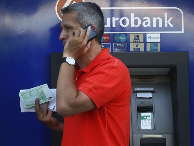 A Greek man holds 100 Euro bills which he just withdrew from a branch of Eurobank in central Athens 