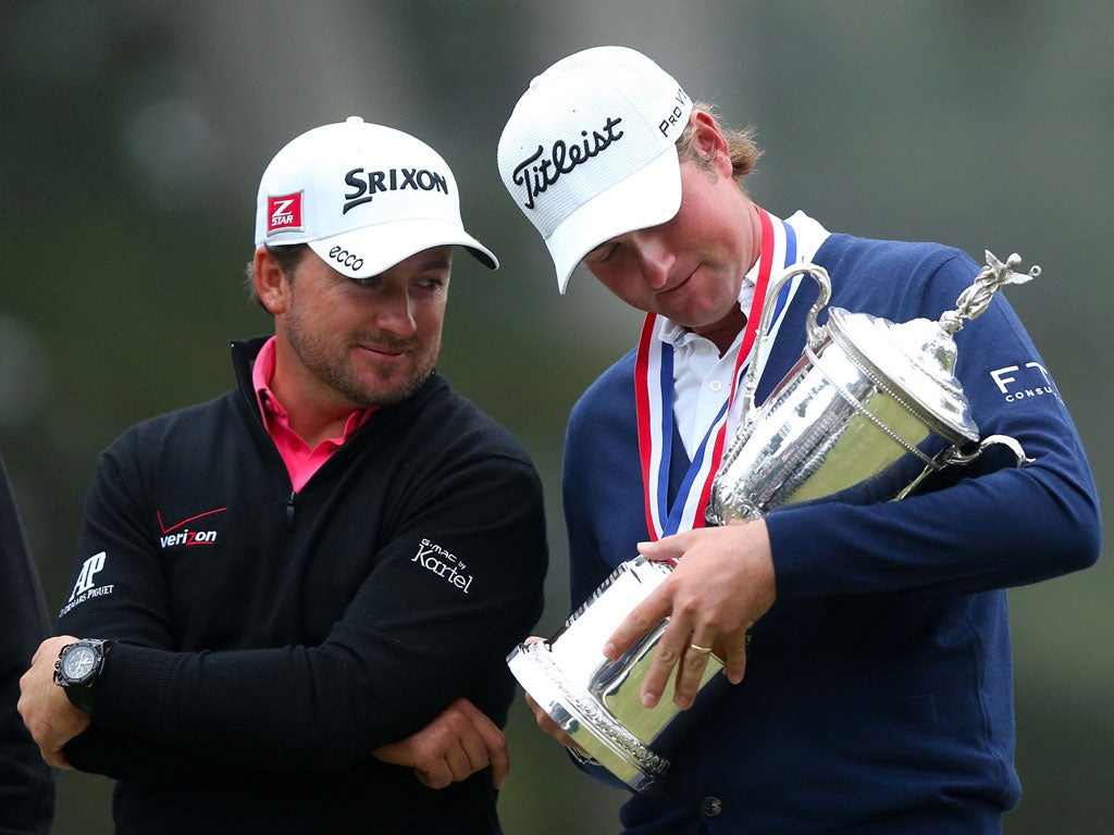 Webb Simpson of the United States (R) looks down at the trophy as Graeme McDowell of Northern Ireland looks on