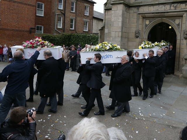 A man leans forward to put a flower on one of the coffins as they are carried out of the church