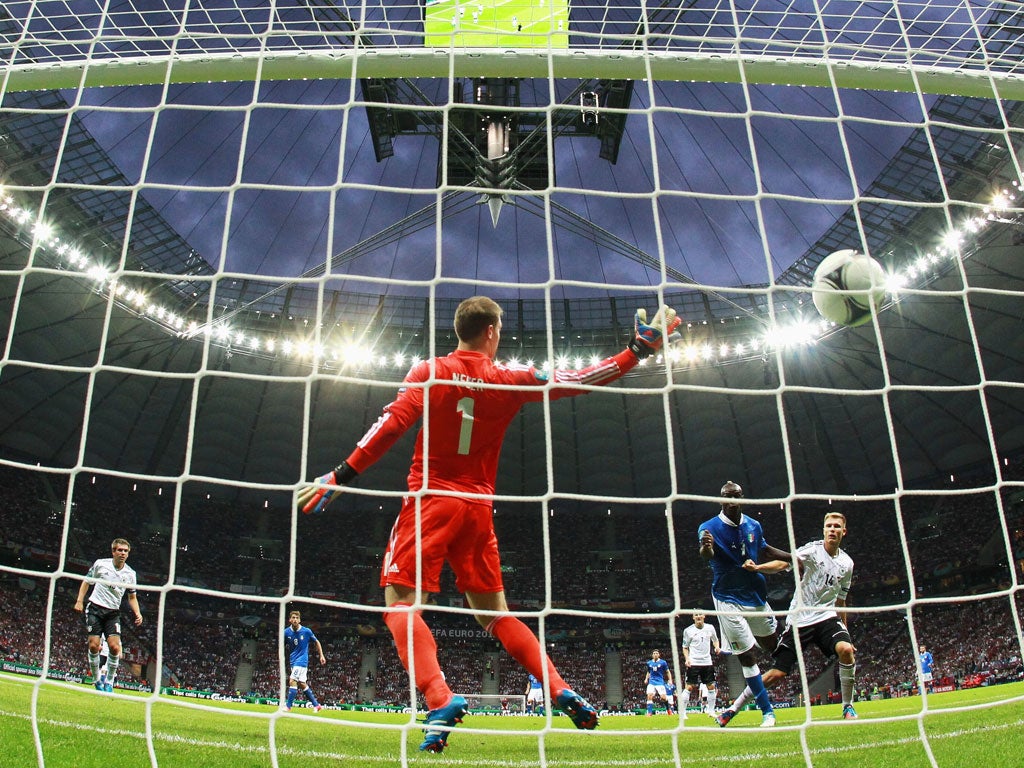 Mario Balotelli of Italy jumps with Holger Badstuber of Germany to score the opening goal past Manuel Neuer