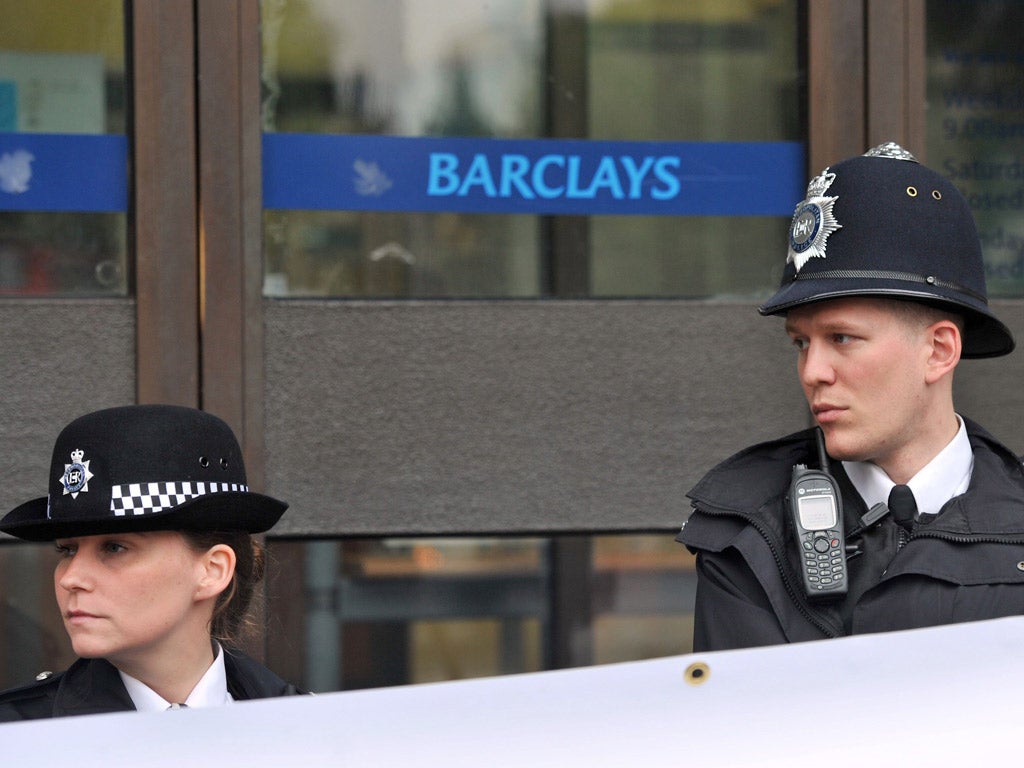 Police officers stand guard at a Barclays branch as activists protest about the Libor scandal