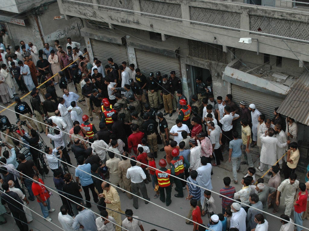 Residents gather outside the house in Lahore where nine cadets training to be prison guards were killed by Taliban gunmen yesterday