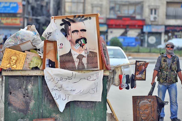 A Syrian rebel stands near a vandalized portrait of Syrian President Bashar al-Assad in the city center of Selehattin, near Aleppo,